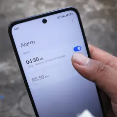 Palec włącza budzik na telefonie. Widzisz ekran z ustawieniami alarmu, jak ustawić budzik w telefonie.
