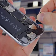 Wymiana baterii w iPhone. Dłoń wyciąga taśmę do demontażu baterii z wnętrza telefonu.