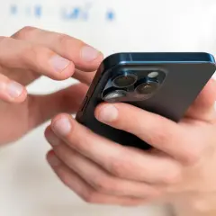Dłonie trzymające ciemny iPhone, na którym można sprawdzić numer IMEI.
