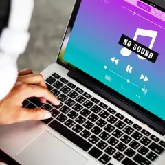 Osoba w słuchawkach próbuje połączyć AirPods z laptopem, ale na ekranie widnieje komunikat "NO SOUND".