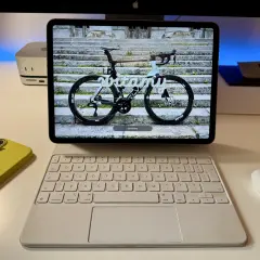 Na ekranie iPada z systemem ipados 26 widoczny jest rower szosowy z napisem "witamy". Obok leży żółty iPhone i biała klawiatura.