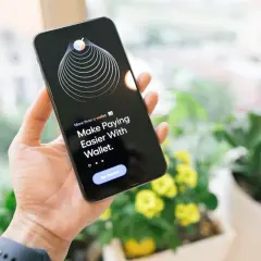 Dłoń trzyma iPhone'a z aplikacją Wallet, która ułatwia płatności dzięki technologii NFC.