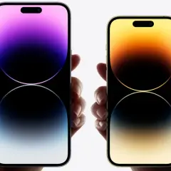 Dwie dłonie trzymają telefony iPhone 16. Jeden z nich ma fioletowy ekran, drugi złoty.