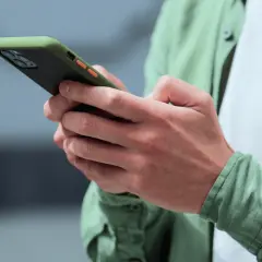 Dłonie trzymające zielono-czarny telefon z pomarańczowymi przyciskami. Może to być powiadomienie z OneSignal.