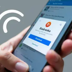 Dłoń trzyma smartfon, na ekranie którego wyświetla się okno pobierania aplikacji Biedronki.
