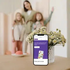 Telefon z aplikacją Bezpieczna Rodzina Play. Mama z córkami w tle.