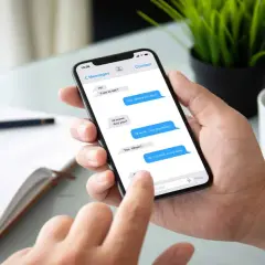 Dłoń trzyma smartfon z widoczną konwersacją SMS. Widać, jak sprawdzić czy sms został odczytany, po niebieskich dymkach wiadomości.