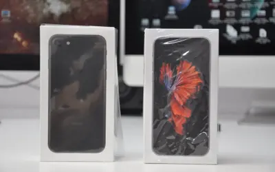 Dwa iPhone'y w pudełkach, jeden czarny, drugi z tapetą z rybką bojownikiem. Nowe telefony z systemem iOS 7.