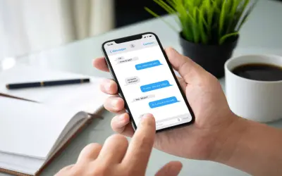 Dłoń trzyma smartfon z widoczną konwersacją SMS. Widać, jak sprawdzić czy sms został odczytany, po niebieskich dymkach wiadomości.
