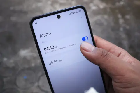 Palec włącza budzik na telefonie. Widzisz ekran z ustawieniami alarmu, jak ustawić budzik w telefonie.
