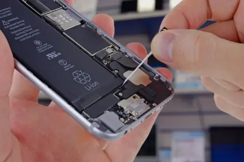 Wymiana baterii w iPhone. Dłoń wyciąga taśmę do demontażu baterii z wnętrza telefonu.