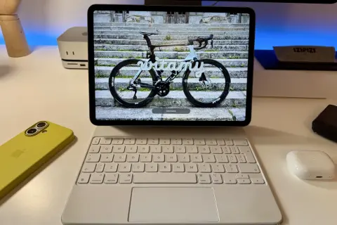 Na ekranie iPada z systemem ipados 26 widoczny jest rower szosowy z napisem "witamy". Obok leży żółty iPhone i biała klawiatura.