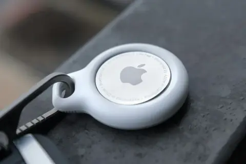 Biały AirTag od Apple, z logo i napisem "Designed by Apple in California". To urządzenie, które pomoże Ci odnaleźć zgubione przedmioty.