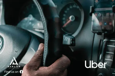 Dłoń kierowcy na kierownicy, obok smartfon z aplikacją Uber.
