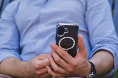 Mężczyzna w niebieskiej koszuli trzyma telefon z widocznym okręgiem, który sugeruje zaawansowaną haptykę.