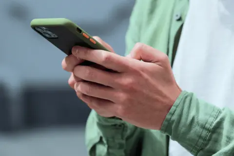 Dłonie trzymające zielono-czarny telefon z pomarańczowymi przyciskami. Może to być powiadomienie z OneSignal.