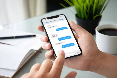 Dłoń trzyma smartfon z widoczną konwersacją SMS. Widać, jak sprawdzić czy sms został odczytany, po niebieskich dymkach wiadomości.
