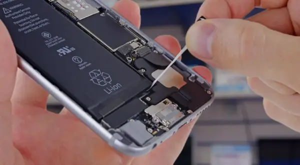 Wymiana baterii w iPhone. Dłoń wyciąga taśmę do demontażu baterii z wnętrza telefonu.