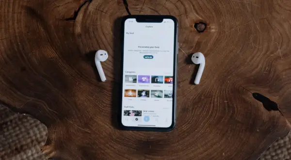 Jak połączyć AirPods z iPhone? Na drewnianym blacie leży iPhone z otwartą aplikacją i dwa białe słuchawki AirPods.