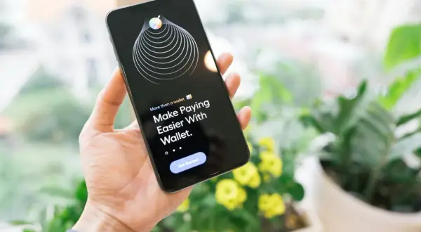 Dłoń trzyma iPhone'a z aplikacją Wallet, która ułatwia płatności dzięki technologii NFC.