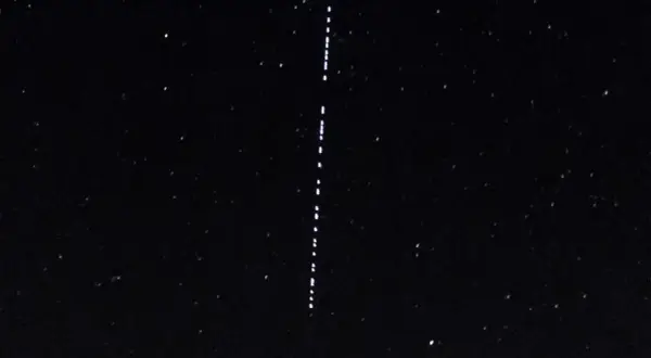 Nocne niebo z gwiazdami i pionowym sznurkiem jasnych punktów, przypominających przeloty Starlink.