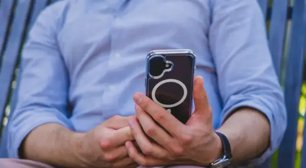 Mężczyzna w niebieskiej koszuli trzyma telefon z widocznym okręgiem, który sugeruje zaawansowaną haptykę.