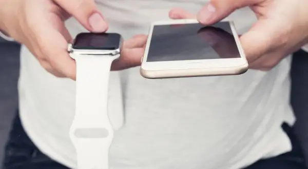 Ręce trzymające Apple Watch i iPhone. Dowiedz się, jak włączyć Apple Watch, parując go z telefonem.
