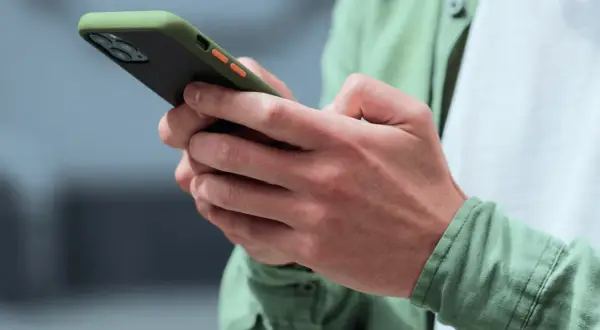 Dłonie trzymające zielono-czarny telefon z pomarańczowymi przyciskami. Może to być powiadomienie z OneSignal.