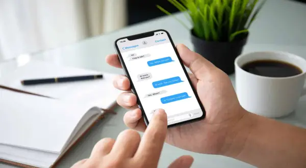 Dłoń trzyma smartfon z widoczną konwersacją SMS. Widać, jak sprawdzić czy sms został odczytany, po niebieskich dymkach wiadomości.
