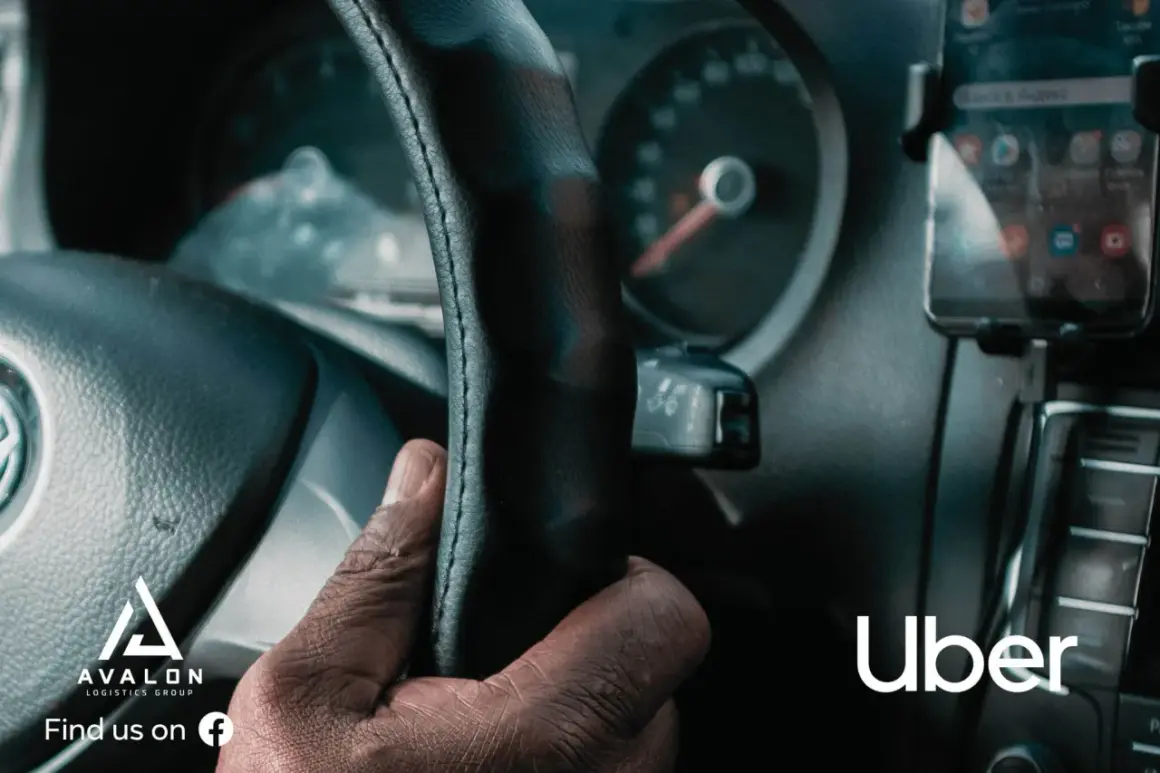 Dłoń kierowcy na kierownicy, obok smartfon z aplikacją Uber.