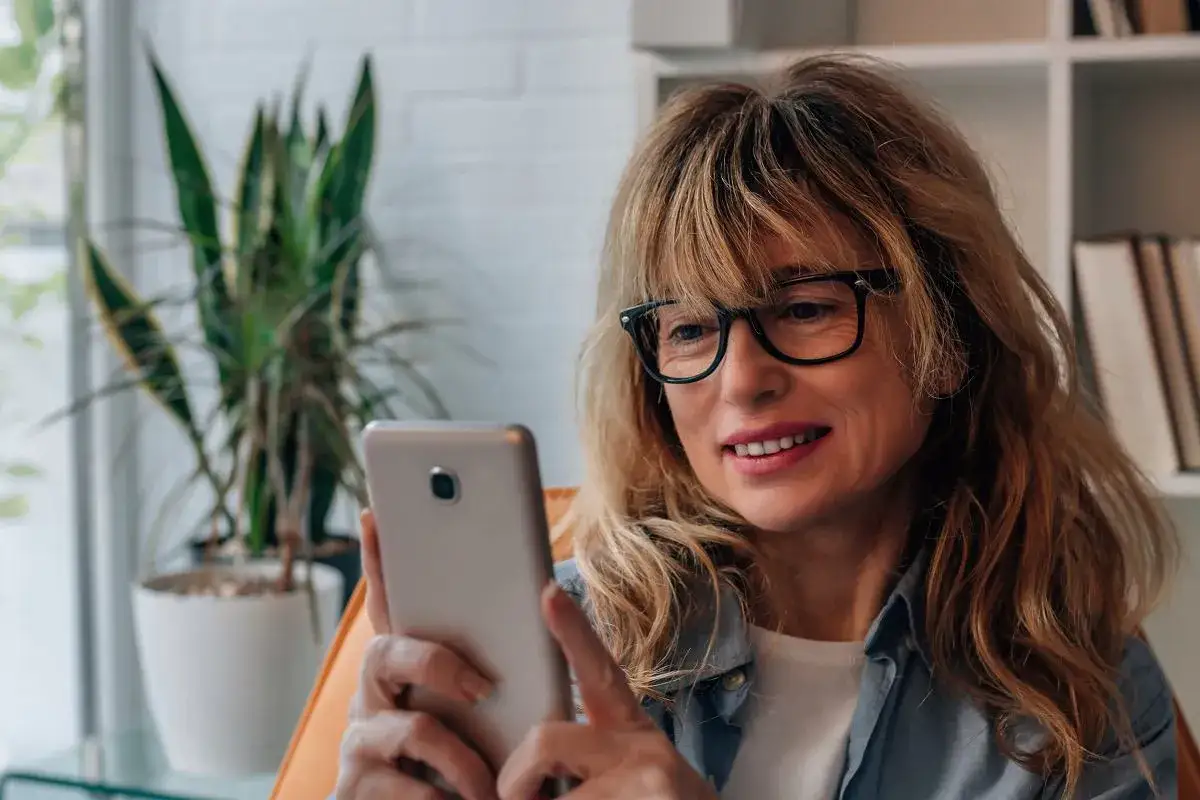 Uśmiechnięta kobieta w okularach korzysta z telefonu, być może szuka bratniej duszy na bumble aplikacja.