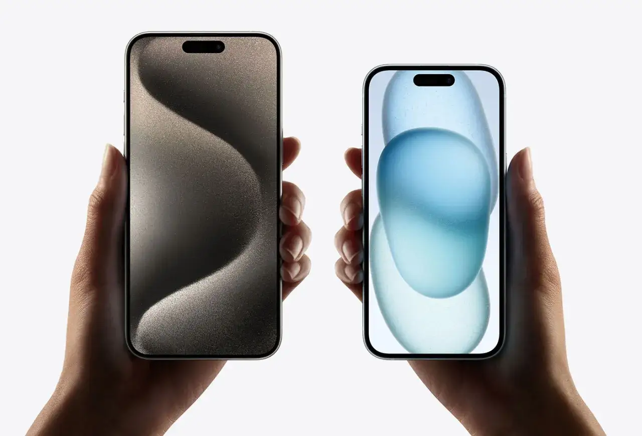 Dwie dłonie trzymają iPhone'y 15. Zastanawiasz się, ile kosztuje wymiana baterii w iPhone 15?