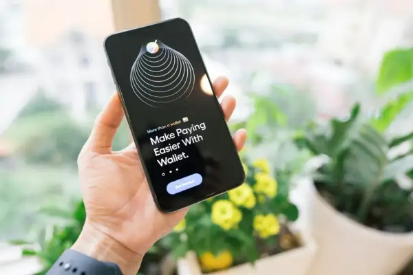 Dłoń trzyma iPhone'a z aplikacją Wallet, która ułatwia płatności dzięki technologii NFC.
