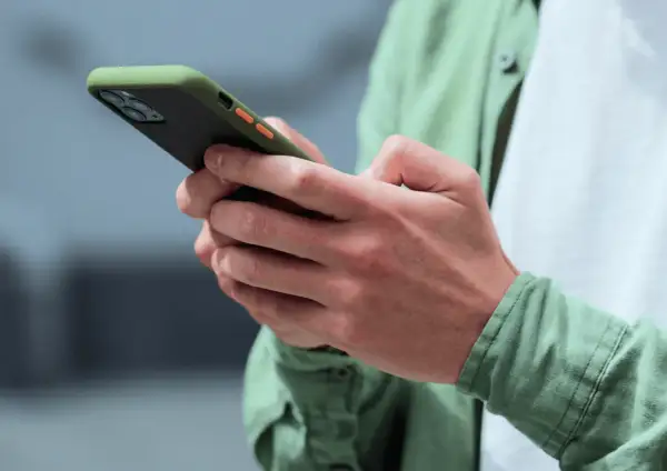 Dłonie trzymające zielono-czarny telefon z pomarańczowymi przyciskami. Może to być powiadomienie z OneSignal.
